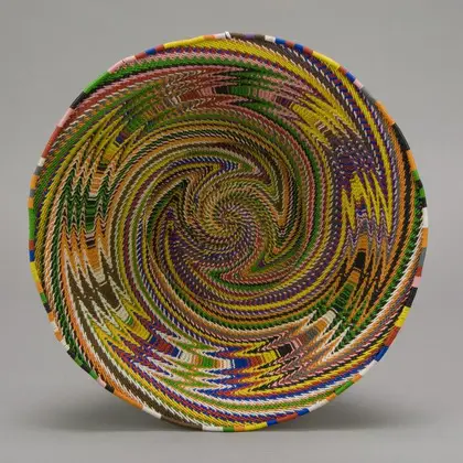 Woven telephone-wire basket with a colorful spiraling multicolor pattern, coiled into a round bowl shape.
