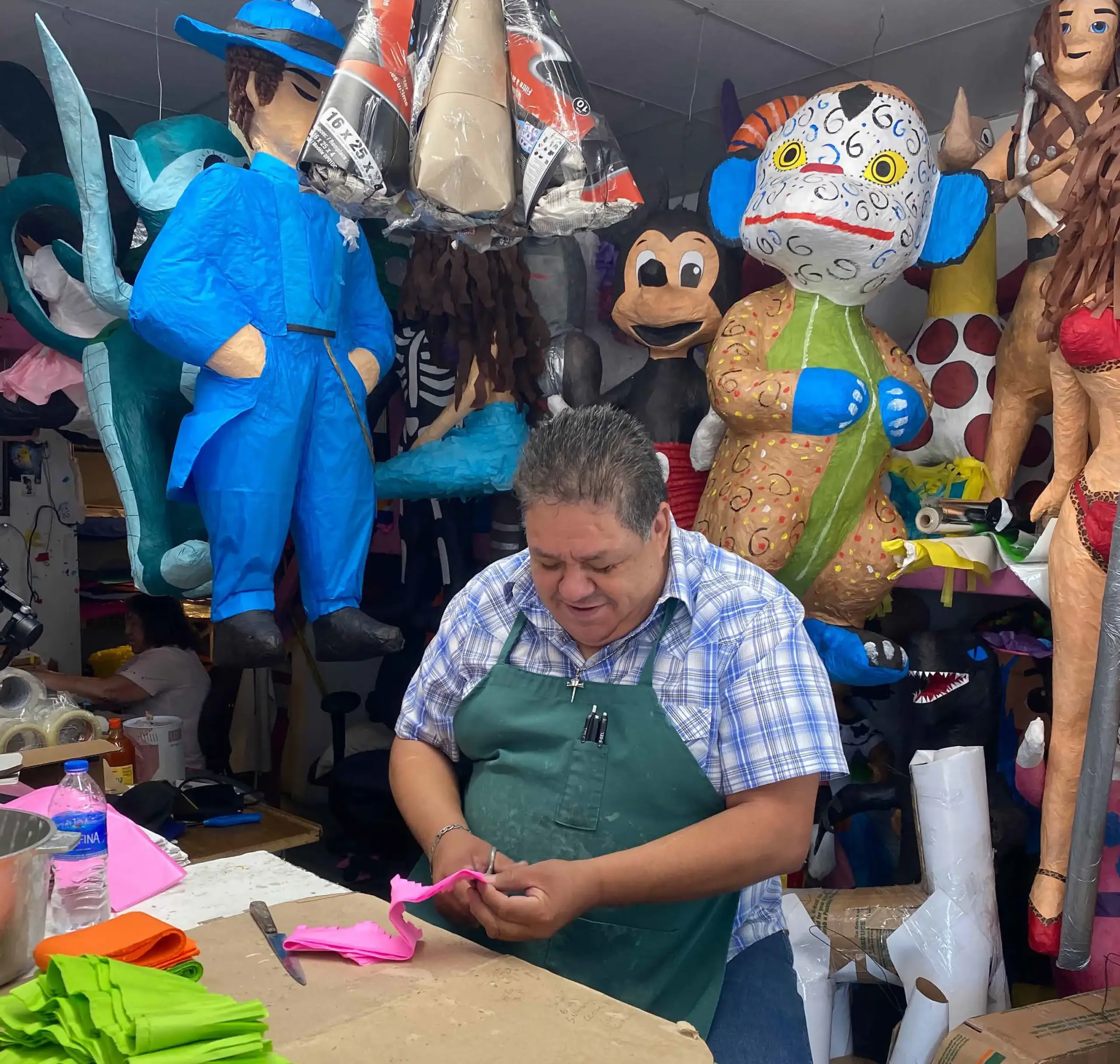 Man wearing a green apron cutting a piece of material to be used on a piñata