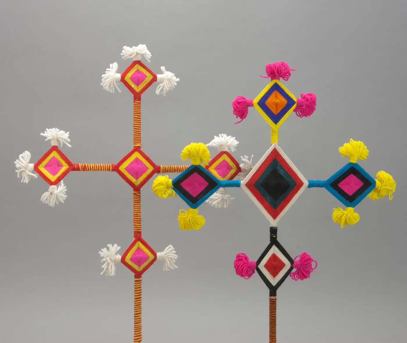 Two multi-diamond God's Eye (ojo de dios) sculptures with colorful yarn-wrapped sticks, tasseled ends, and layered concentric patterns.