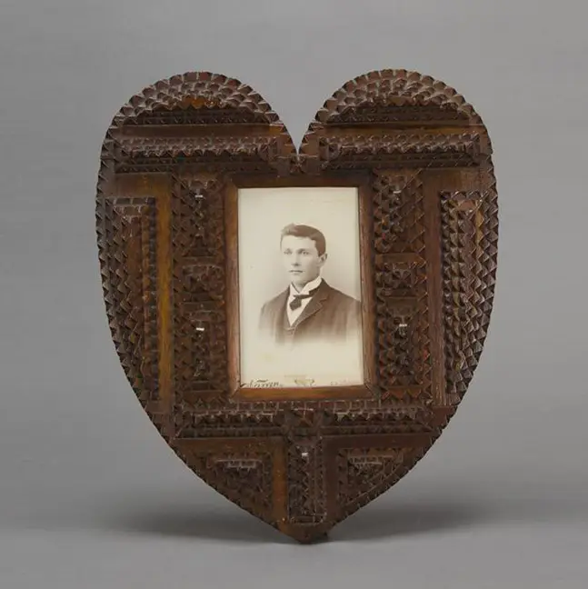 Heart-shaped tramp art picture frame with chip-carved wooden layers, holding a vintage sepia photograph of a young man.
