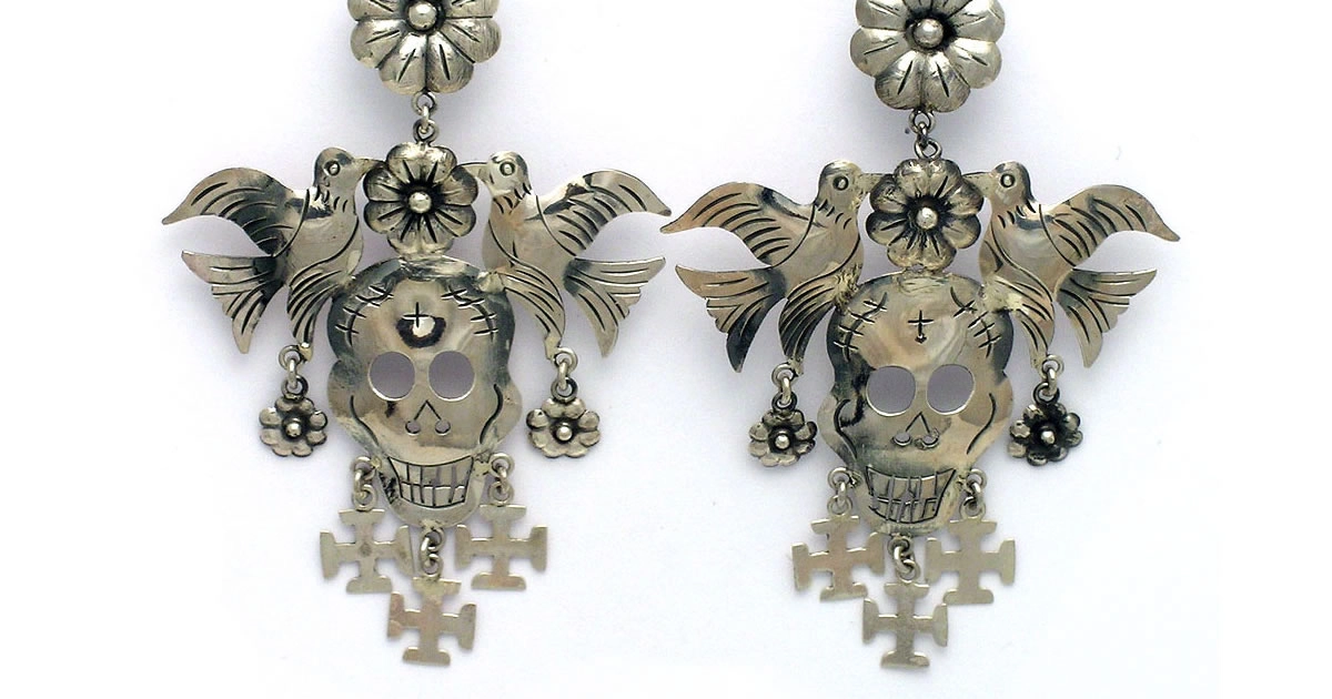 online-shop A pair of silver drop earrings featuring engraved sugar skulls flanked by birds and flowers