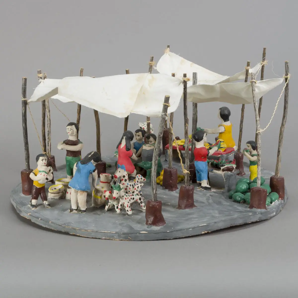 A miniature circular dance stage with a white canopy and wooden posts, populated by colorful figurines dancing around the edge.